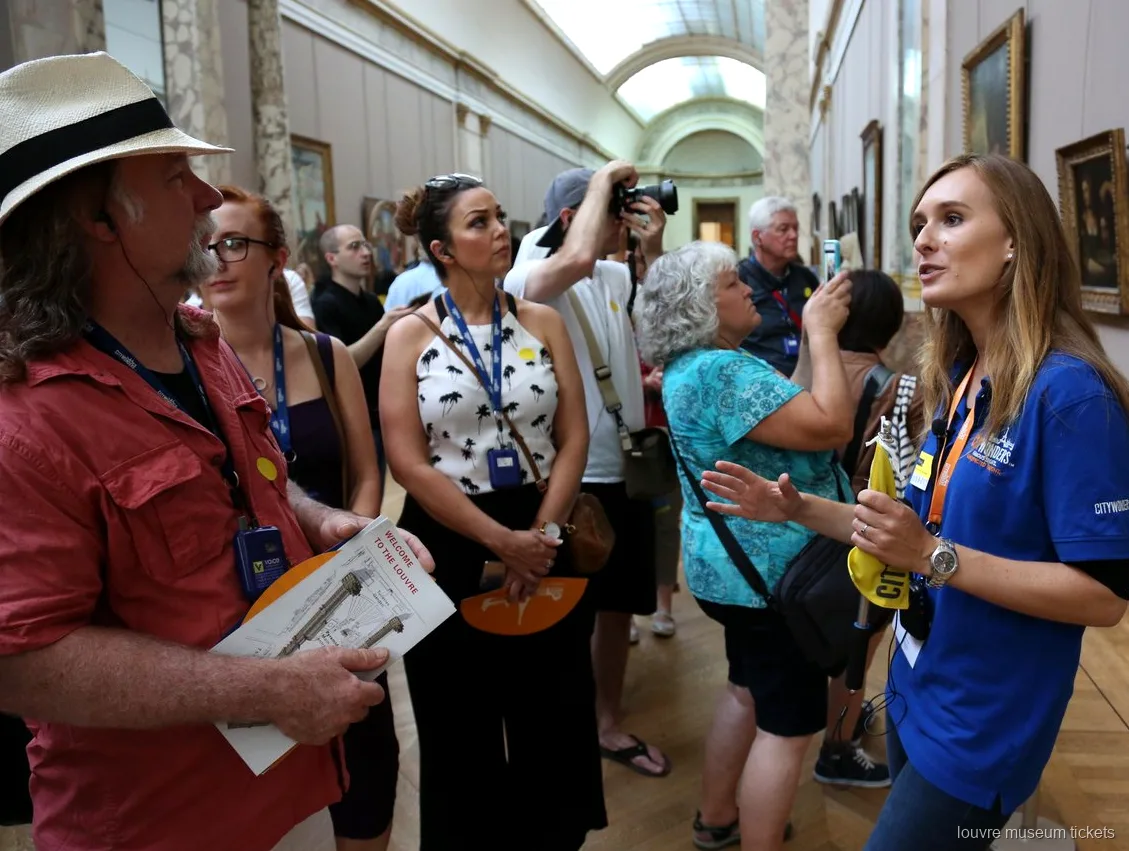 Guida in maglia blu che parla a un gruppo con le mappe del Louvre in galleria, tour con biglietti Museo del Louvre