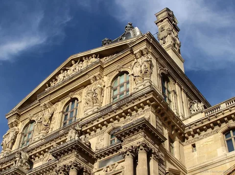 Carved Louvre facade with statues, pediment and columns under a deep blue sky, seen with Louvre Museum tickets