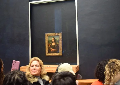 Visitantes ante la Mona Lisa tras el cristal en la pared oscura de la sala, con entradas Museo del Louvre