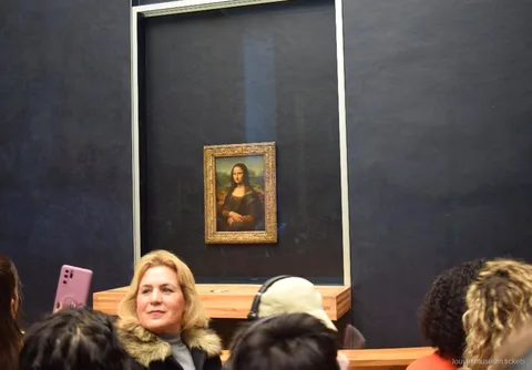 Visiteurs devant la Joconde derrière sa vitre sur le mur sombre de la salle, temps fort avec billets musée du Louvre